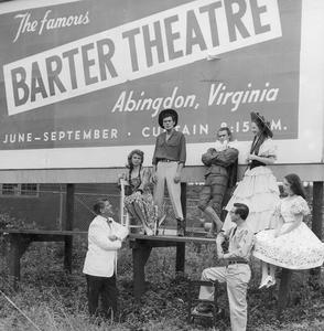 A group of actors pose with Bob in front of a Barter billboard.