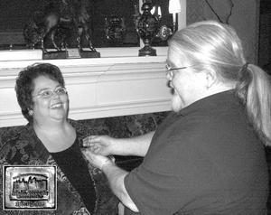 MainStreet: Greeneville Board President Kathy Knight smiles as James-Ben Stockton presents her with a sterling 25th Year Celebration lapel pin. 