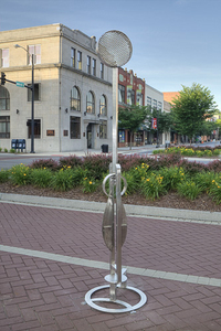 Dr. Marvin Tadlock's eight-foot-tall "Moire" is a stainless steel kinetic piece. It bends with the wind similar to a weather vane except that it moves to right itself when the wind dies. It has two patterns at the top where movement reflects moire patterns. 